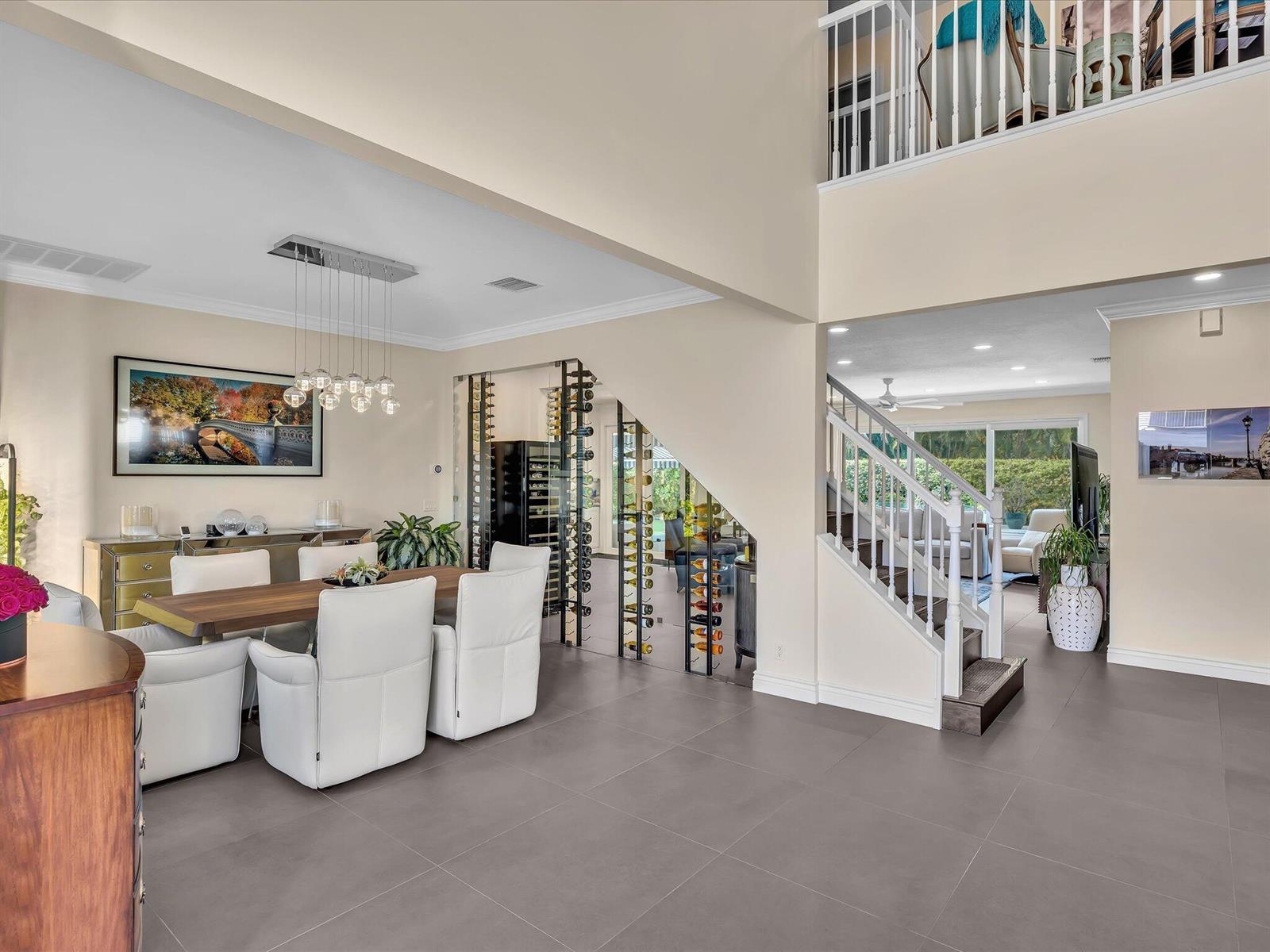 A dining area with a glass wine rack sits beside a staircase in an open-concept home — 4770 Glenn Pine Lane, Boynton Beach FL 33436, BOYNTON BEACH, FL