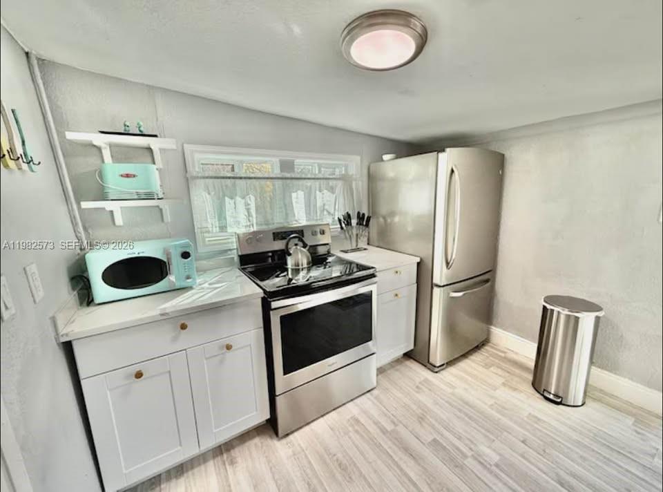 A small kitchen features white cabinets, stainless steel appliances, and light-colored wood-look flooring — 213 N E St, Lake Worth FL 33460, LAKE WORTH, FL