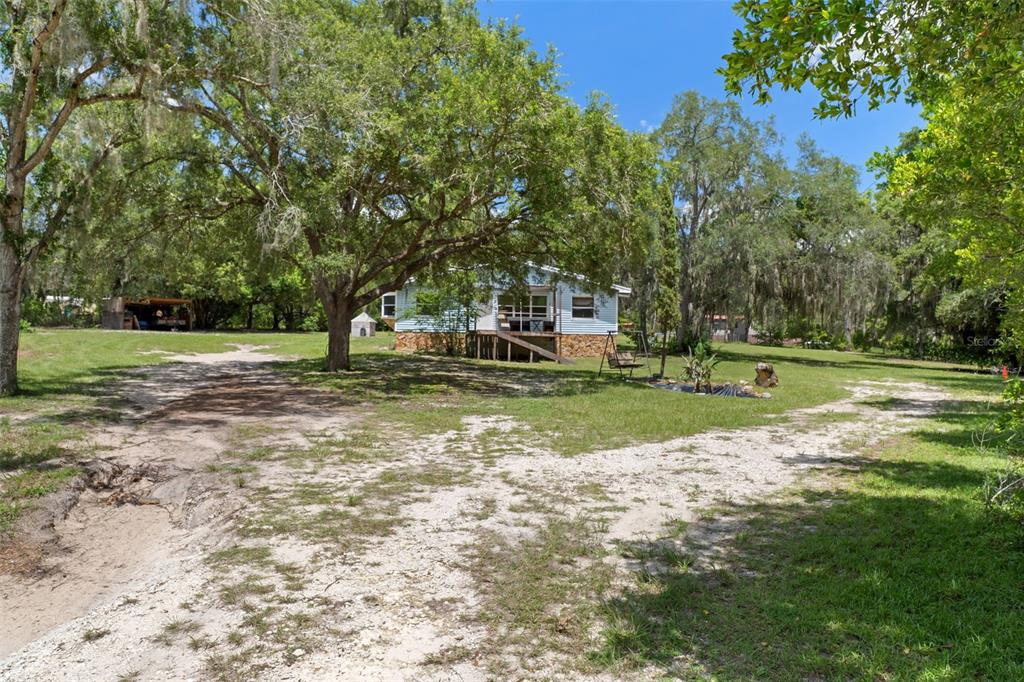 A light blue house sits on a large, grassy lot with mature trees and dirt paths — 12042 KAMBACK DRIVE, BROOKSVILLE, FL