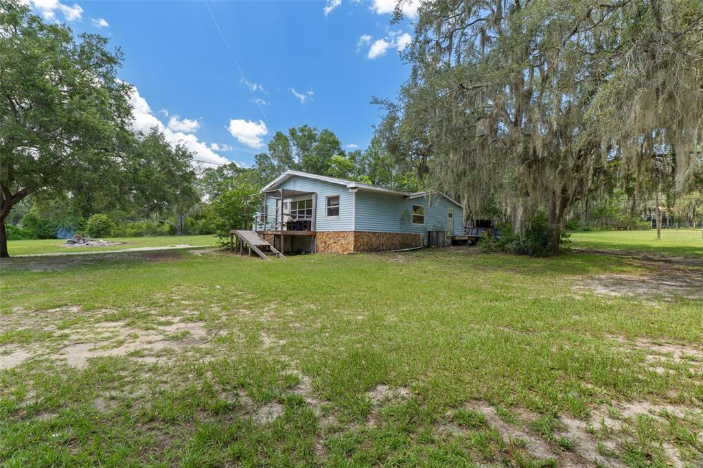 A light blue single-story house with a wooden deck stands on a grassy lot — 12042 KAMBACK DRIVE, BROOKSVILLE, FL