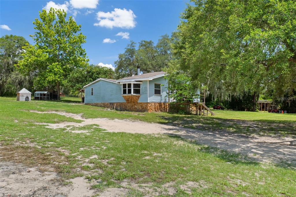 A light blue house with a stone foundation sits on a large, grassy, sandy lot — 12042 KAMBACK DRIVE, BROOKSVILLE, FL