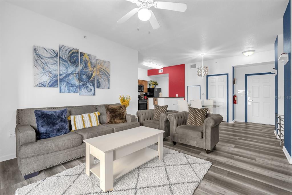 A living room with a grey sofa, two armchairs, a coffee table, and abstract wall art — 8112 POINCIANA BLVD UNIT 1214, ORLANDO, FL