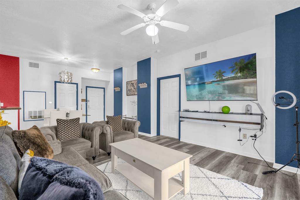 A living room features a large wall-mounted television, gray sofas, and a white coffee table — 8112 POINCIANA BLVD UNIT 1214, ORLANDO, FL