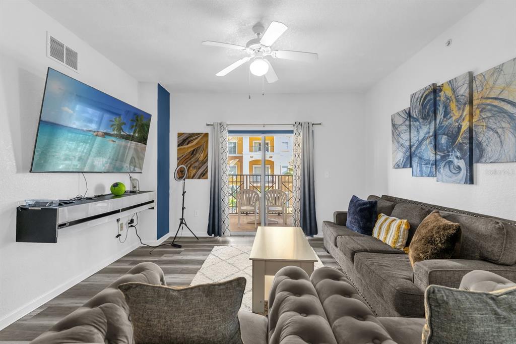 A living room features a wall-mounted television, a gray sofa, and a balcony with chairs — 8112 POINCIANA BLVD UNIT 1214, ORLANDO, FL