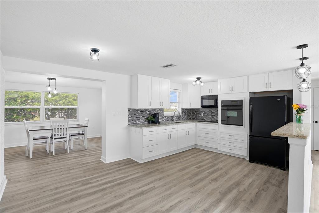 A kitchen with white cabinets, granite countertops, and a dining area with light wood flooring — 10737 FILLMORE AVENUE, PORT RICHEY, FL