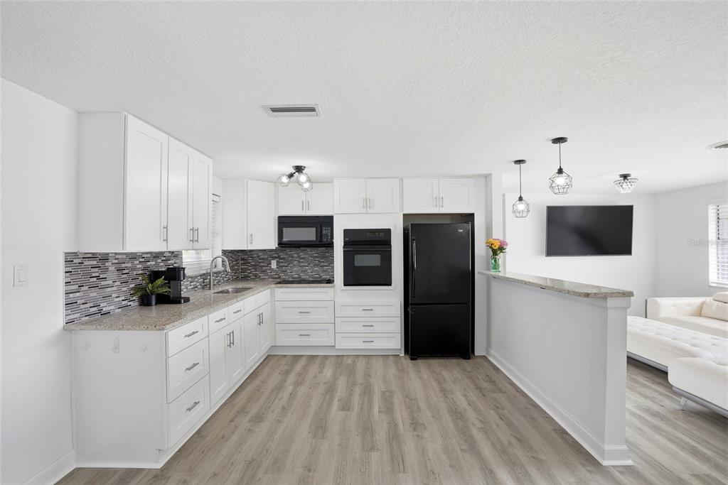 A kitchen with white cabinets, black appliances, granite countertops, and wood-look flooring — 10737 FILLMORE AVENUE, PORT RICHEY, FL