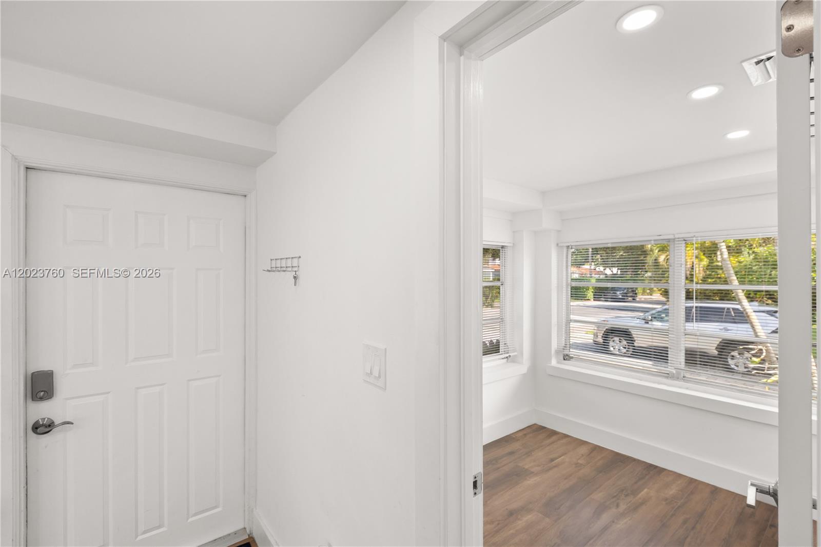 A white door opens into a room with wood-look flooring and large windows — 900 Tangier St, Coral Gables FL 33134, CORAL GABLES, FL