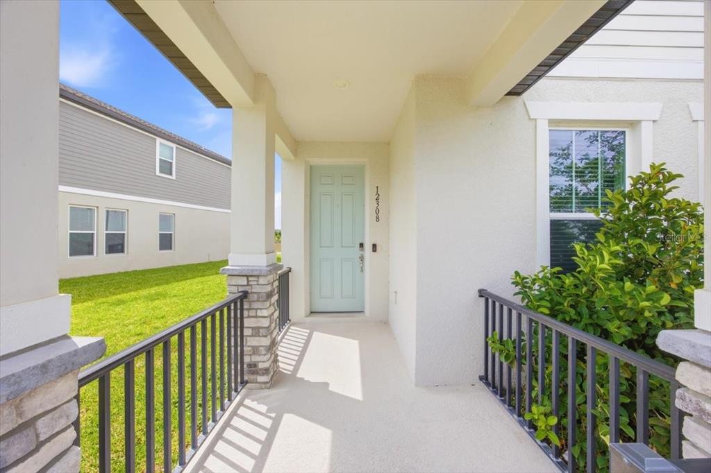 A covered front porch features a light blue door, stone-based columns, and black metal railings — 12308 BRACCO STREET, WINTER GARDEN, FL