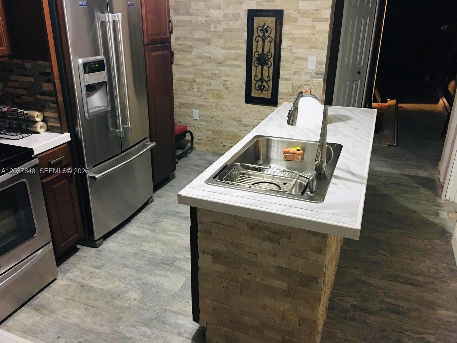 A kitchen island with a sink and marble-look countertop sits before a stone-tiled wall — 6424 Meade St, Hollywood FL 33024, HOLLYWOOD, FL