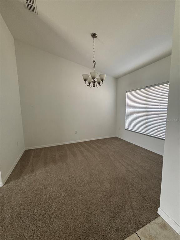 An empty dining room features beige carpet, white walls, and a hanging chandelier — 4030 MARINA ISLE DRIVE, KISSIMMEE, FL