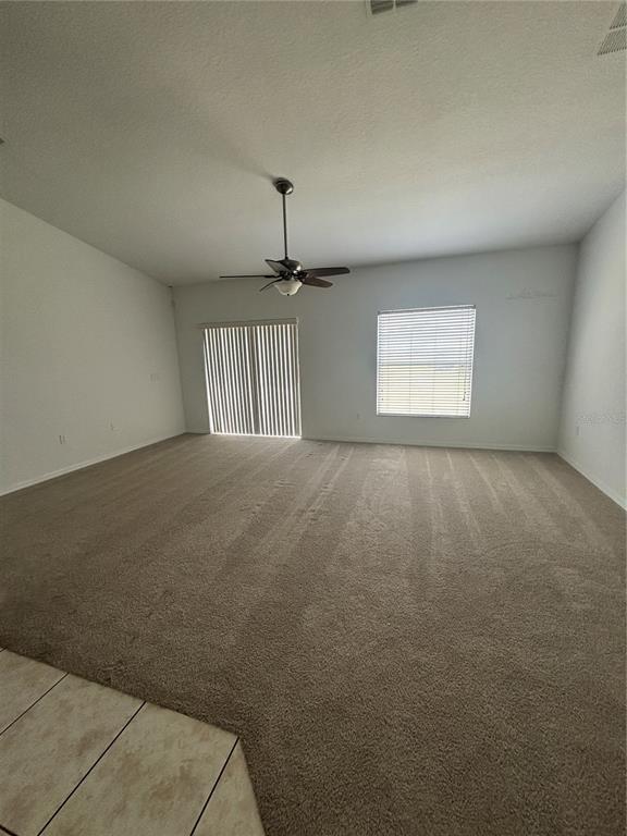 An empty living room features beige carpeting, a ceiling fan, and a sliding glass door — 4030 MARINA ISLE DRIVE, KISSIMMEE, FL