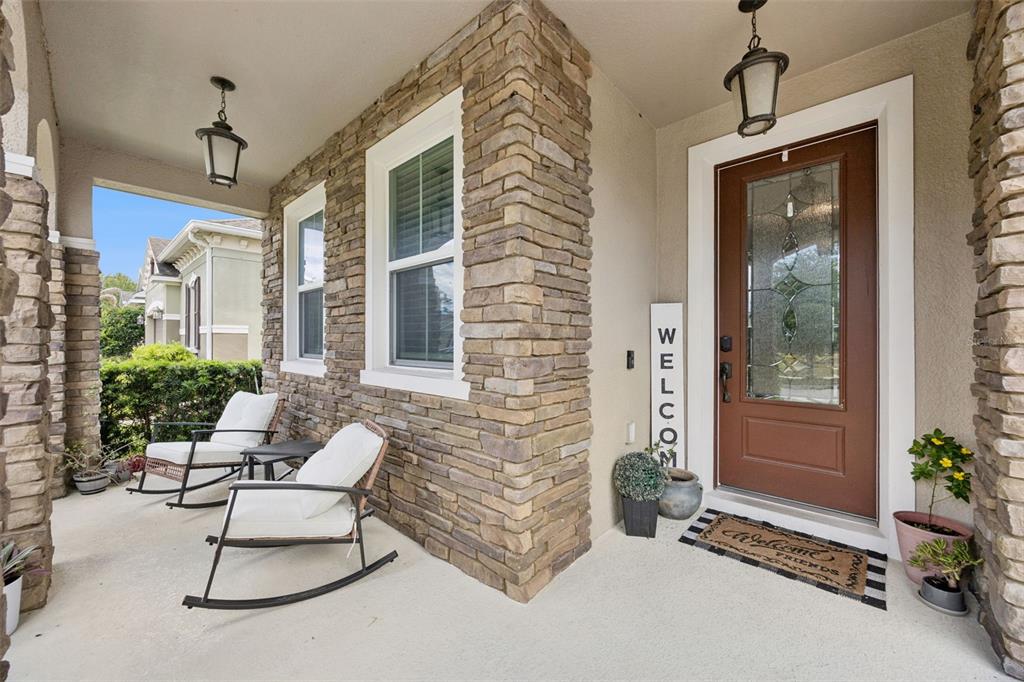 A covered front porch features stone pillars, two rocking chairs, and a brown front door — 2331 AVELLINO AVENUE, ST CLOUD, FL