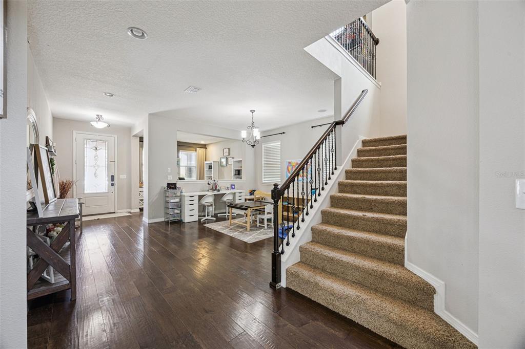 An entryway features dark wood flooring, a carpeted staircase with iron railings, and a desk area — 2331 AVELLINO AVENUE, ST CLOUD, FL