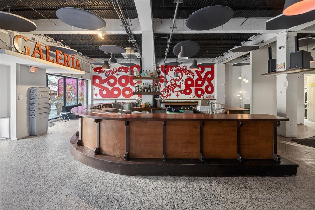 A curved wooden bar sits in a room with industrial ceilings and red wall murals — 722 CALLE CERRA, SAN JUAN, PR