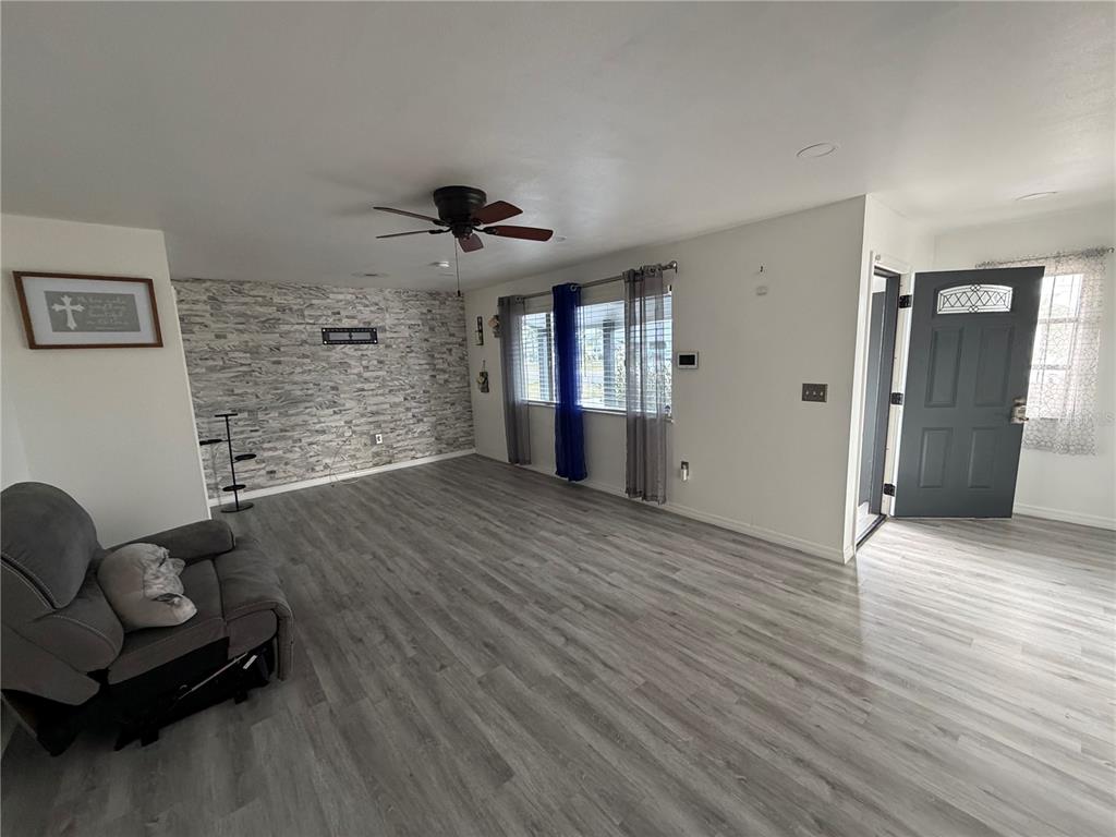 A living room features gray wood-look flooring, a stone-accent wall, and a dark gray door — 1205 HACIENDA DRIVE, SUN CITY CENTER, FL