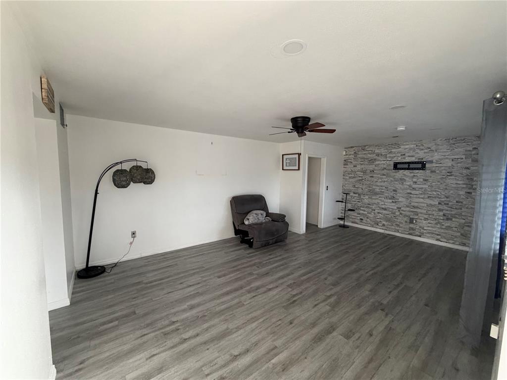 A living room with gray wood-look flooring, a stone accent wall, and a ceiling fan — 1205 HACIENDA DRIVE, SUN CITY CENTER, FL