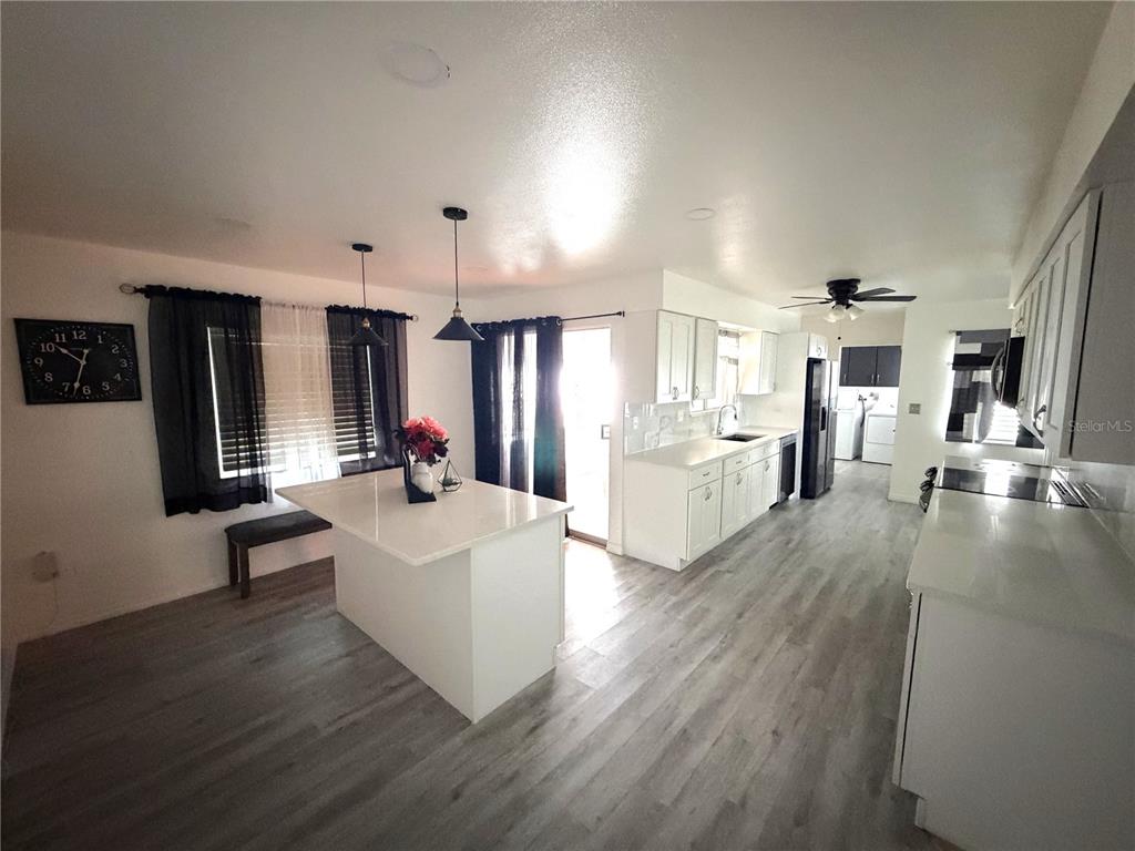 A modern kitchen features white cabinetry, a central island, and light wood-look flooring — 1205 HACIENDA DRIVE, SUN CITY CENTER, FL