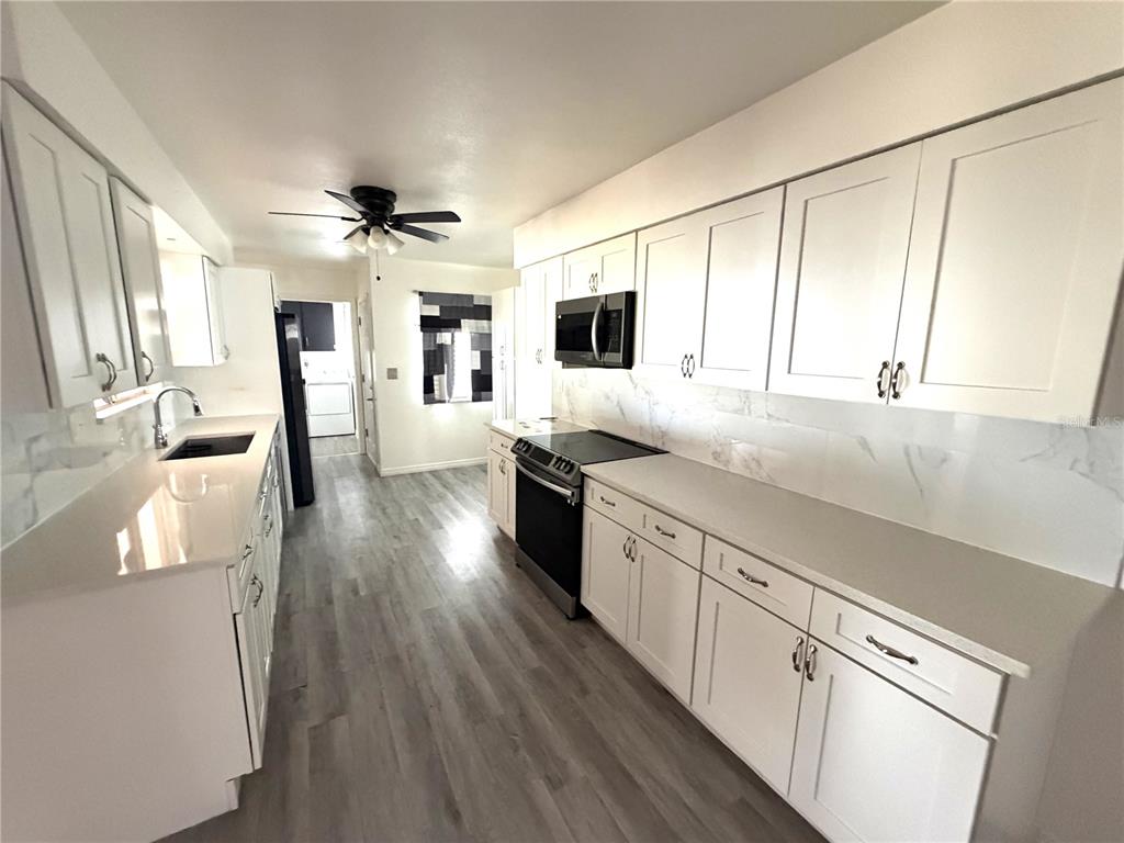 A galley-style kitchen features white cabinets, stainless steel appliances, and light wood-look flooring — 1205 HACIENDA DRIVE, SUN CITY CENTER, FL