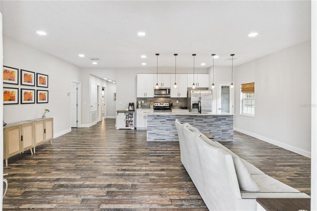 An open-concept kitchen and living area features white cabinetry, a stone-tiled island, and wood-look flooring — 945 GORDON AVENUE, BARTOW, FL