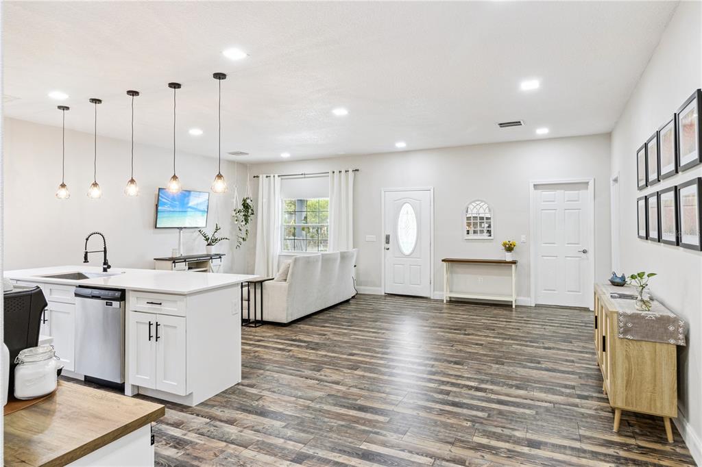 An open-concept kitchen and living area features white cabinetry, pendant lighting, and wood-look flooring — 945 GORDON AVENUE, BARTOW, FL