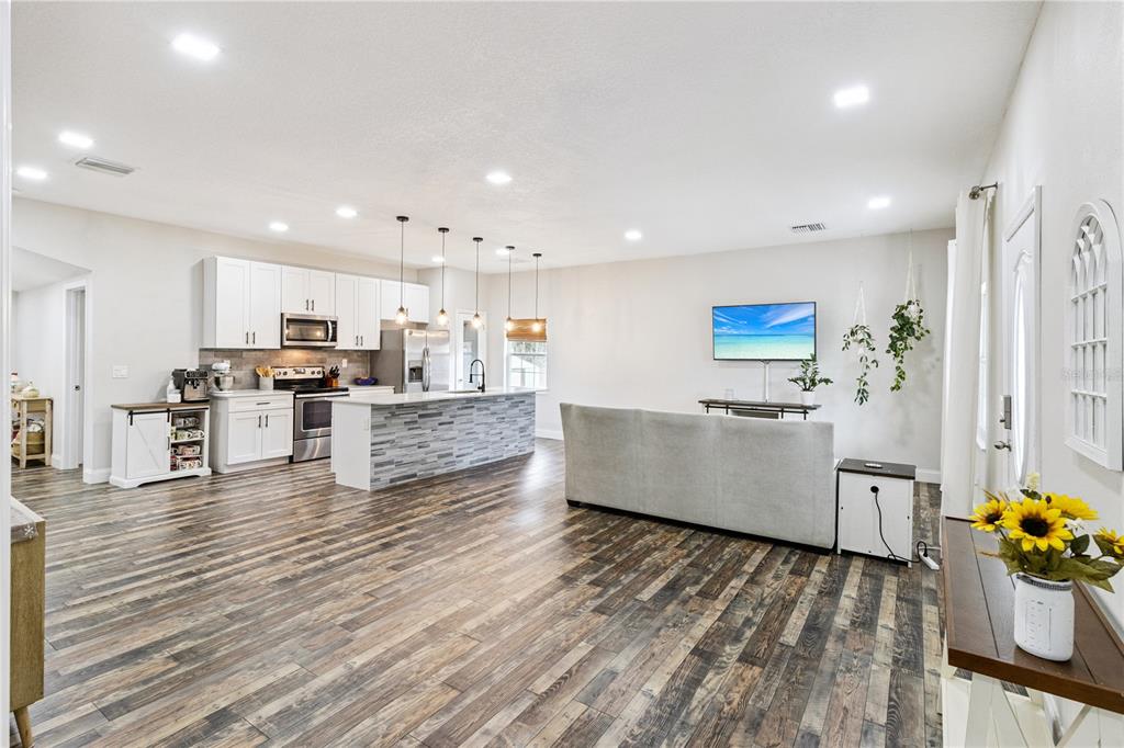 An open-concept kitchen and living area features white cabinetry, a stone-tiled island, and wood-look flooring — 945 GORDON AVENUE, BARTOW, FL