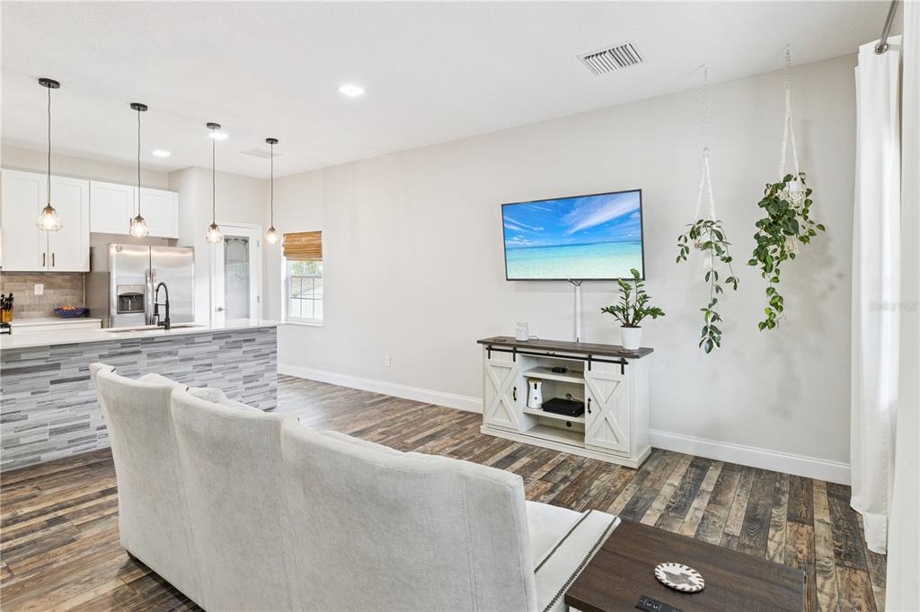 A living room with wood-look flooring, a wall-mounted television, and an open kitchen area — 945 GORDON AVENUE, BARTOW, FL