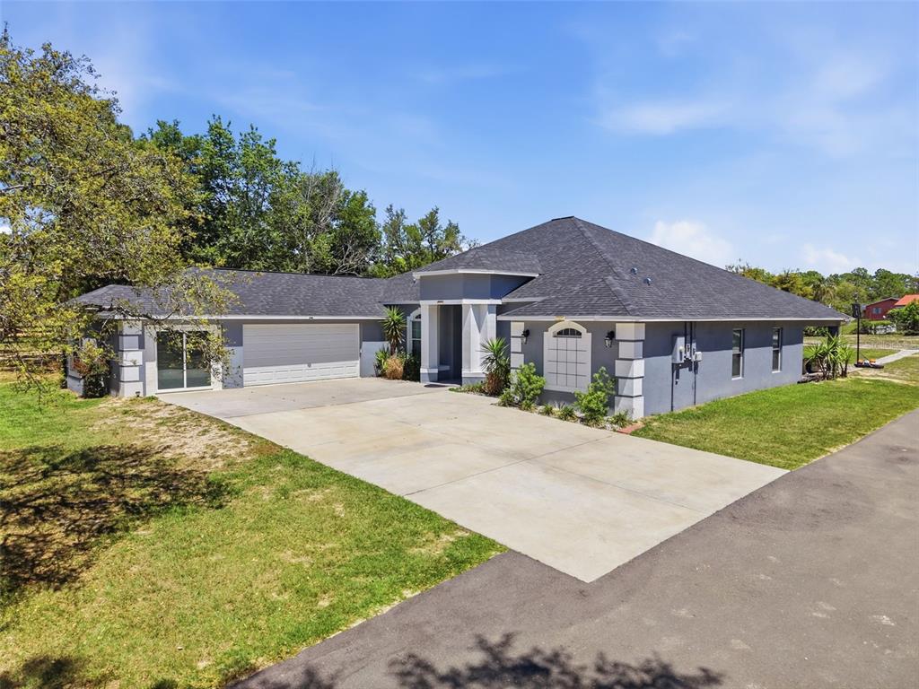 A gray single-story house with a dark shingled roof, a two-car garage, and a driveway — 18354 MONTEVERDE DRIVE, SPRING HILL, FL