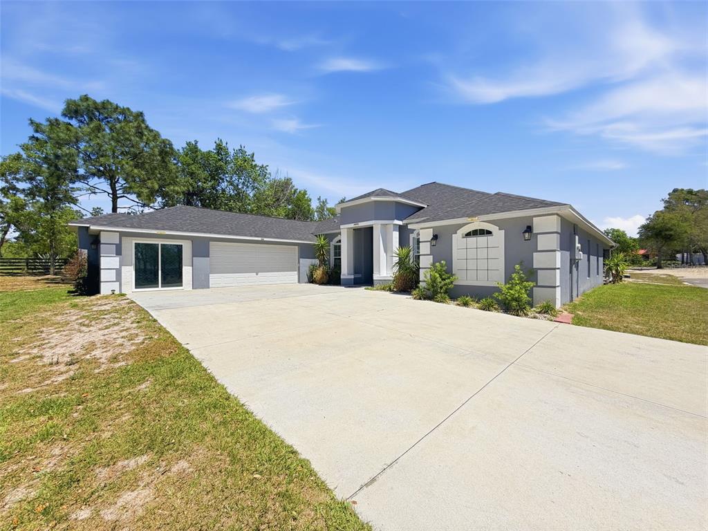 A gray single-story house features a large concrete driveway, a two-car garage, and white trim — 18354 MONTEVERDE DRIVE, SPRING HILL, FL
