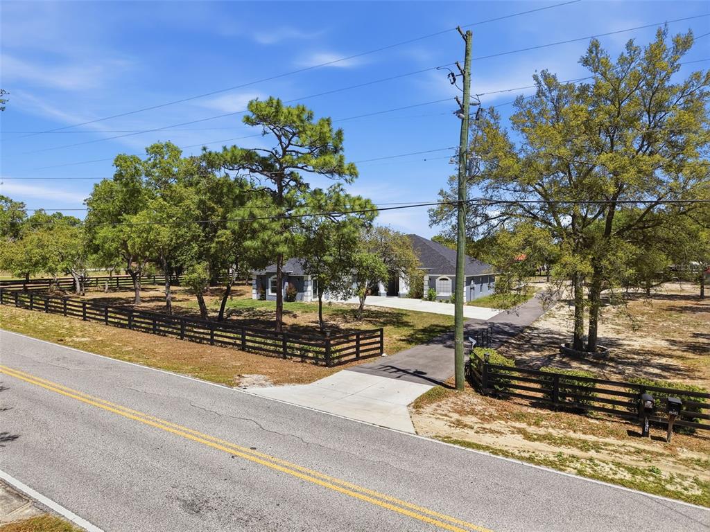 An exterior view of a house set back from a road behind a wooden fence — 18354 MONTEVERDE DRIVE, SPRING HILL, FL