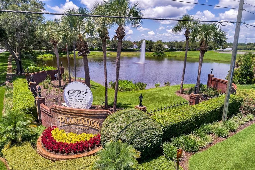 An exterior view of a brick entrance sign for The Plantation Golf Club near a pond — 25308 CASA DEL LAGO LANE, LEESBURG, FL