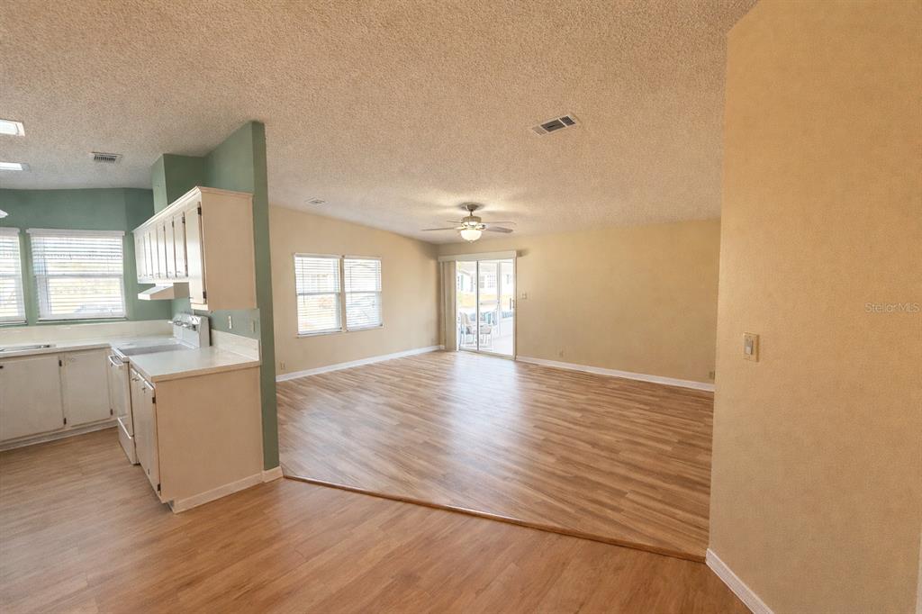 An open-concept living area features light wood-look flooring, beige walls, and a kitchen with white cabinets — 25308 CASA DEL LAGO LANE, LEESBURG, FL