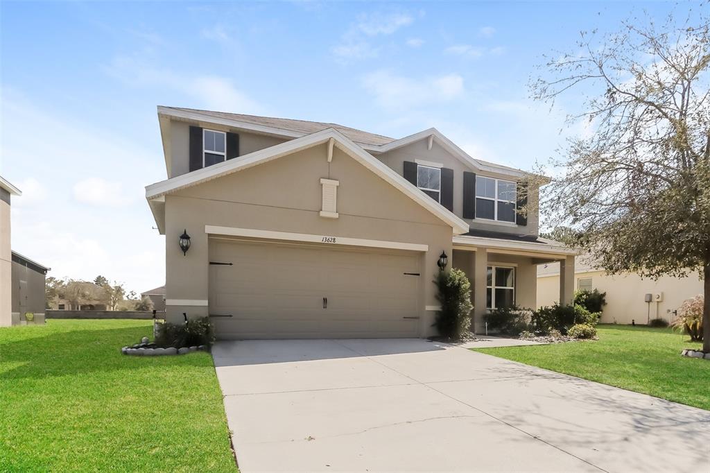A two-story suburban house with a tan stucco exterior and a two-car garage — 13628 COVEY RUN PLACE, SPRING HILL, FL