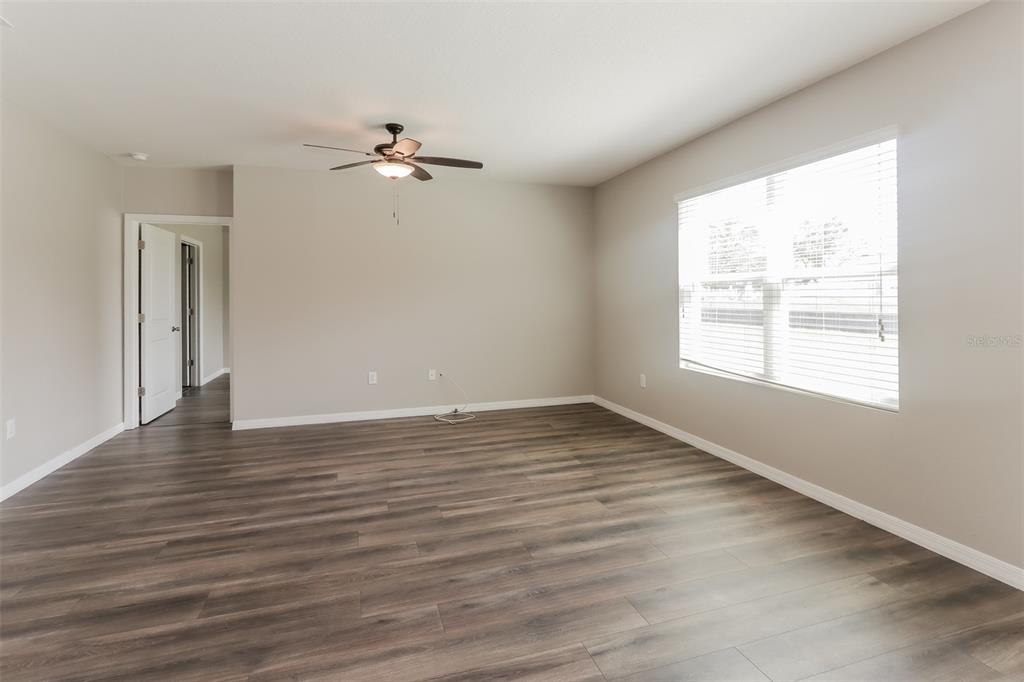 An empty room features wood-look flooring, a ceiling fan, and a large window with blinds — 13628 COVEY RUN PLACE, SPRING HILL, FL