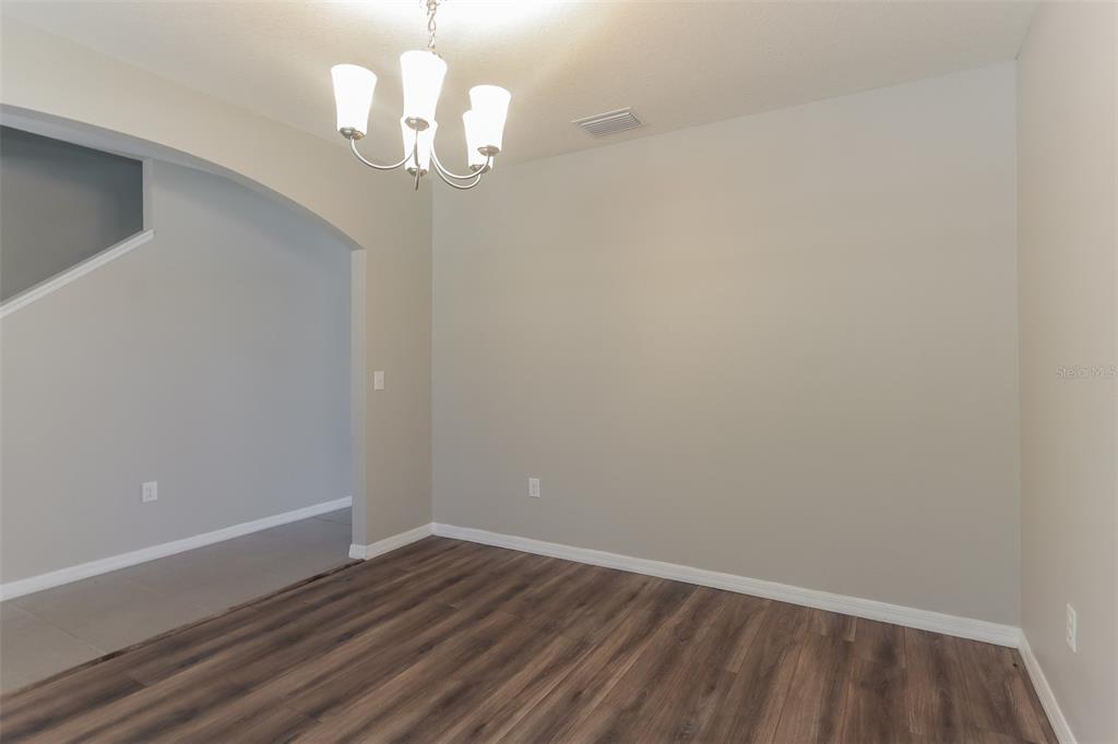 An empty dining room features wood-look flooring, light gray walls, and a hanging chandelier — 13628 COVEY RUN PLACE, SPRING HILL, FL