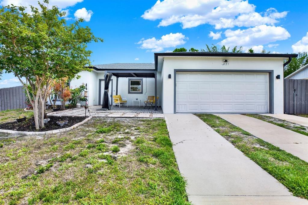 A single-story house with a white exterior, a two-car garage, and a paved patio area — 3023 MUIR STREET, HOLIDAY, FL