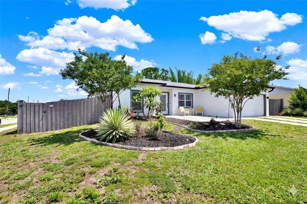 A single-story white house features a front yard with landscaping, a fence, and two trees — 3023 MUIR STREET, HOLIDAY, FL