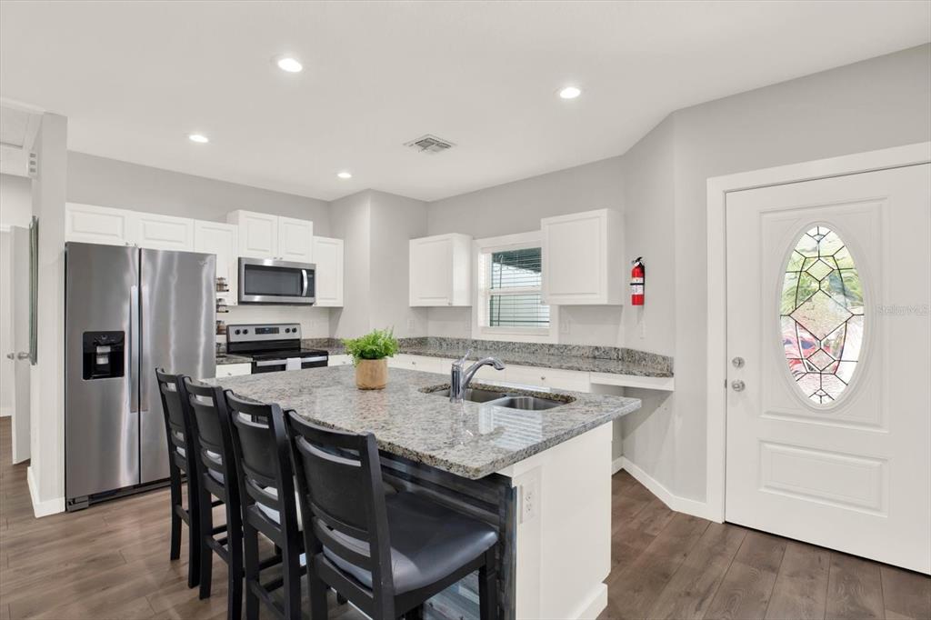 A kitchen with white cabinets, granite countertops, a center island with seating, and stainless appliances — 3023 MUIR STREET, HOLIDAY, FL