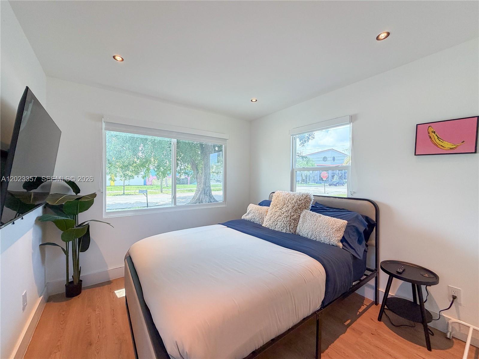 A bedroom features a bed with blue and white bedding, a wall-mounted television, and windows — 105 SW 4th Ave # 0, Hallandale Beach FL 33009, HALLANDALE BEACH, FL