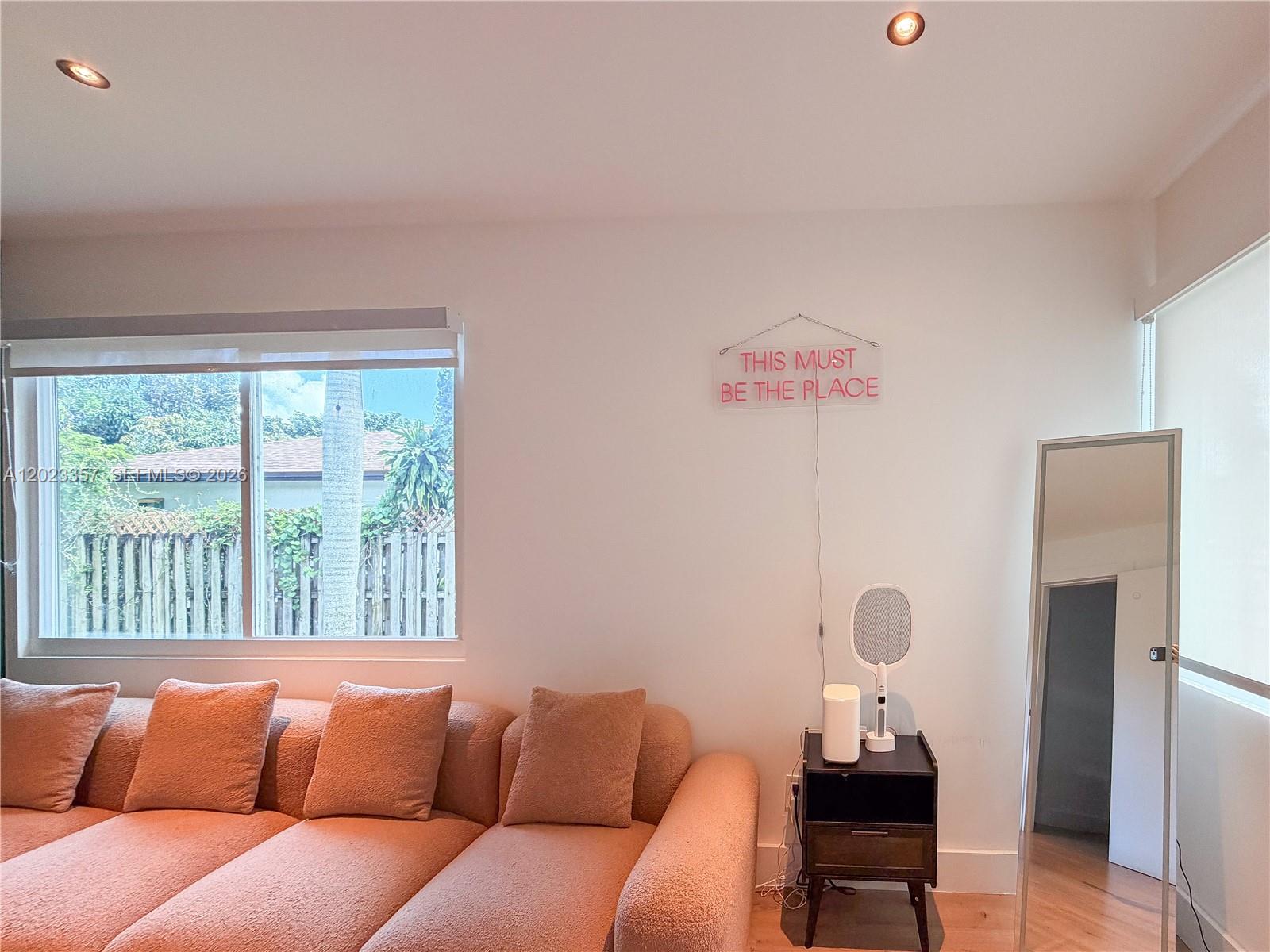 A living room features a textured peach sofa, a neon wall sign, and a floor mirror — 105 SW 4th Ave # 0, Hallandale Beach FL 33009, HALLANDALE BEACH, FL