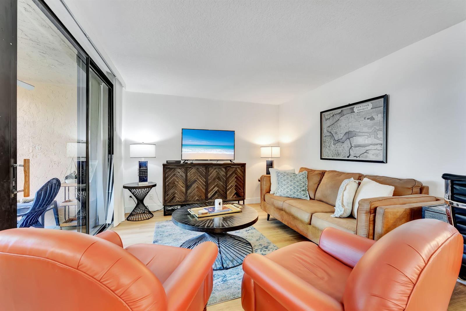 A living room features a brown leather sofa, two orange armchairs, and a television console — 955 Dotterel Road # 2103, Delray Beach FL 33444, DELRAY BEACH, FL