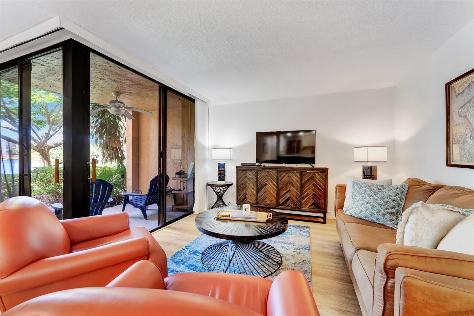 A living room features a leather sofa, orange armchairs, a coffee table, and a sliding door — 955 Dotterel Road # 2103, Delray Beach FL 33444, DELRAY BEACH, FL