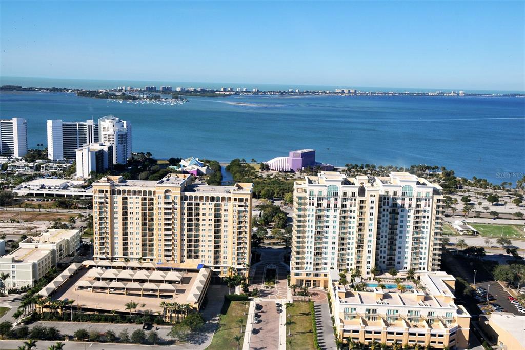 An aerial view shows two large residential buildings near a bay with a distant coastline — 750 N TAMIAMI TRAIL UNIT 205, SARASOTA, FL