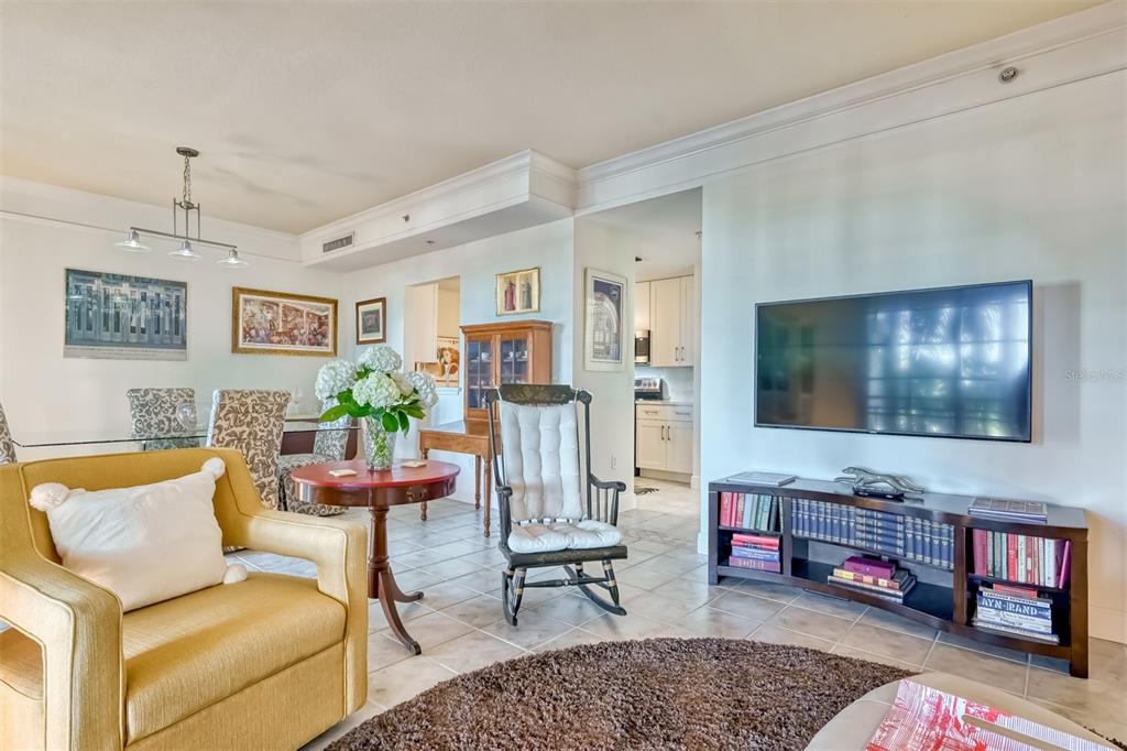 A living room with a yellow armchair, a television, a bookshelf, and a dining area — 750 N TAMIAMI TRAIL UNIT 205, SARASOTA, FL