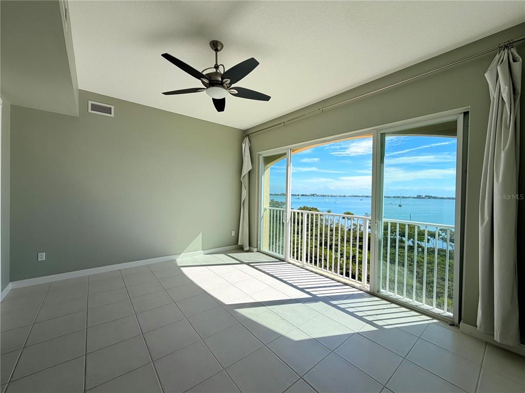 An empty room with light-colored tile flooring, a ceiling fan, and sliding glass doors overlooking water — 29 HARBOUR ISLE UNIT PH01, HUTCHINSON ISLAND, FL