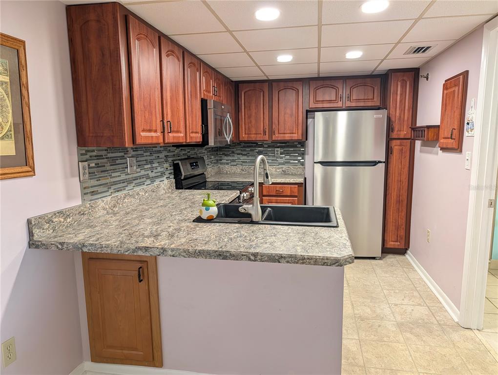 A kitchen features wood cabinets, a patterned laminate countertop, a black sink, and stainless appliances — 3006 CARING WAY UNIT 209, PORT CHARLOTTE, FL