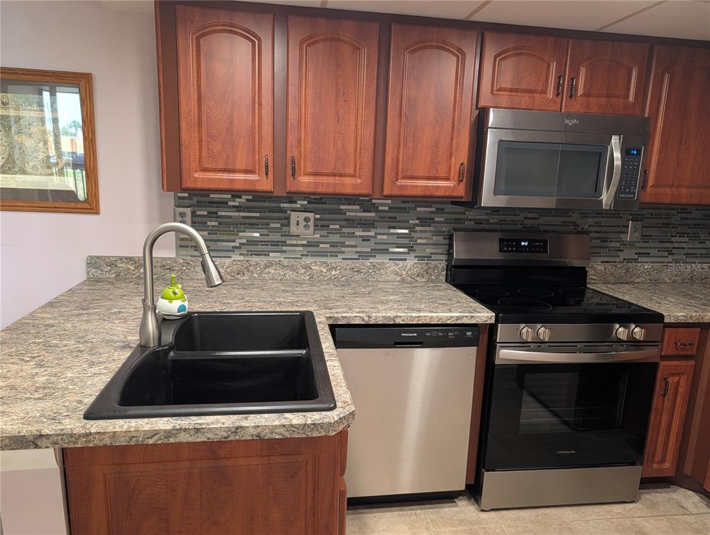 A kitchen features wood cabinets, laminate countertops, a black sink, and stainless steel appliances — 3006 CARING WAY UNIT 209, PORT CHARLOTTE, FL