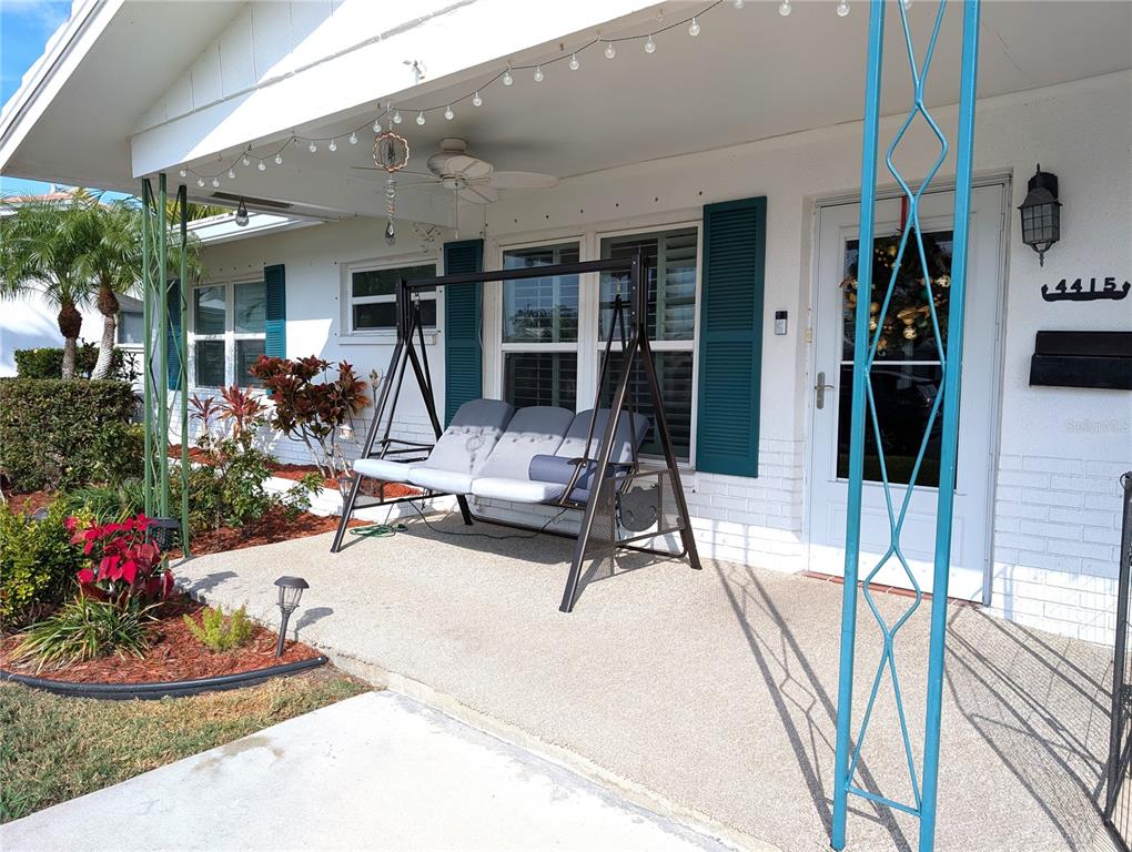 A white house exterior features a covered porch with a swing and teal shutters — 4415 96TH AVENUE N, PINELLAS PARK, FL