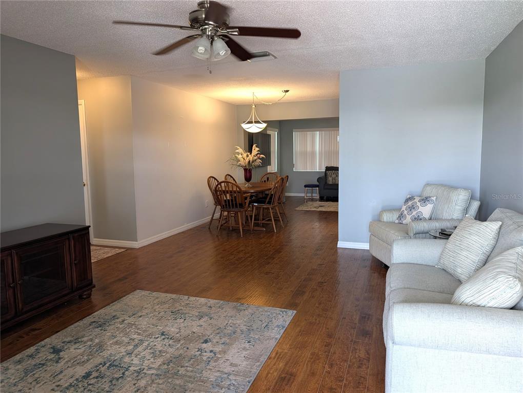 A living room and dining area feature hardwood floors, light gray walls, and ceiling fans — 4415 96TH AVENUE N, PINELLAS PARK, FL