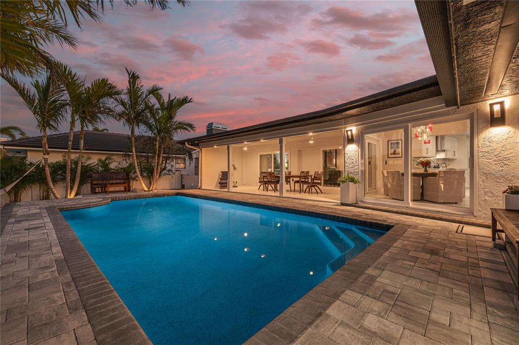 A backyard swimming pool with a stone patio sits beside a house with sliding doors — 4959 58TH AVENUE S, ST PETERSBURG, FL