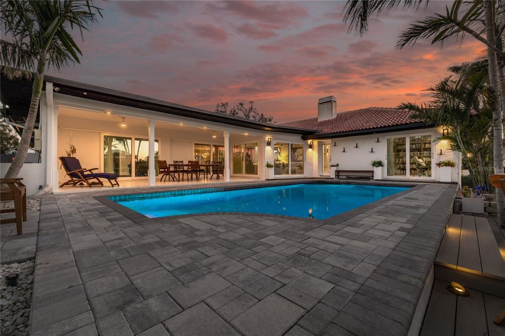 A backyard swimming pool with a paved deck and a covered patio at sunset — 4959 58TH AVENUE S, ST PETERSBURG, FL